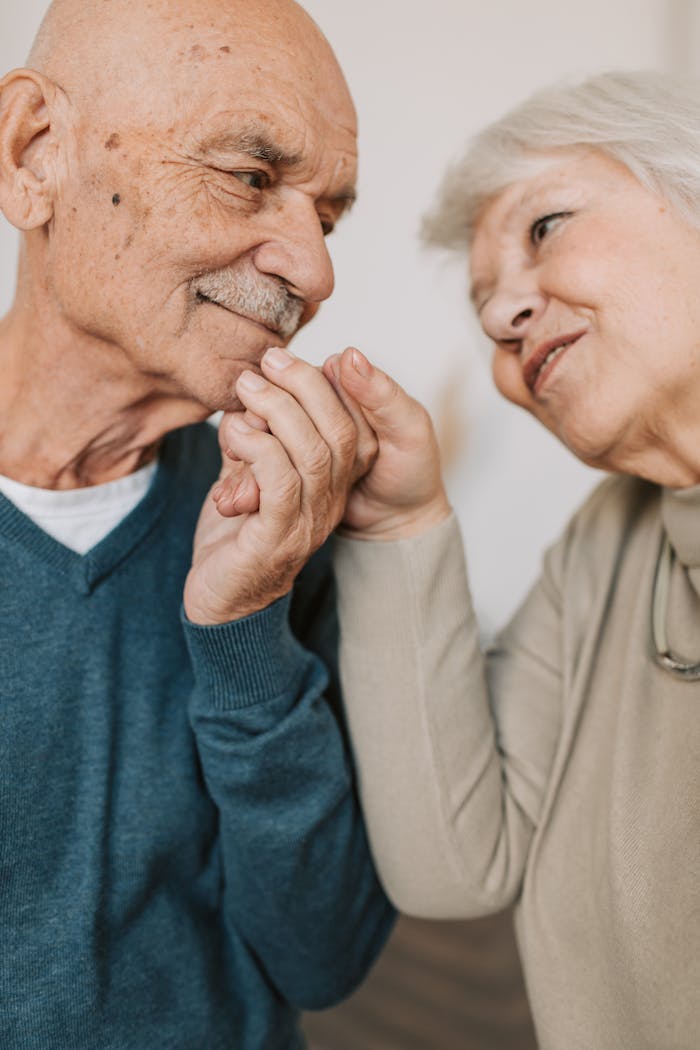 An elderly couple expressing love and affection, holding hands indoors.