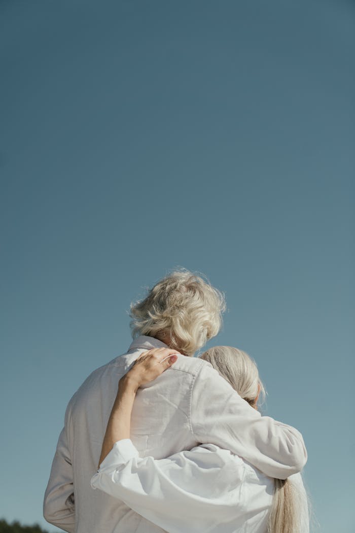 A senior couple hugs tenderly outdoors under a serene sky, symbolizing love and companionship.
