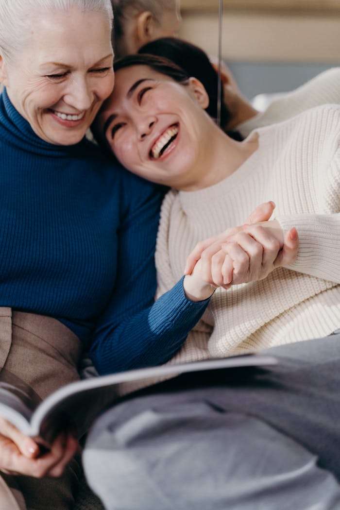 Two women, an adult and a senior adult, laugh together while reading a book indoors.