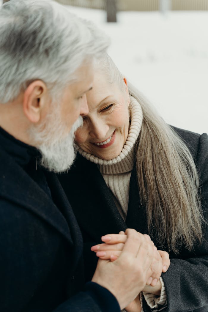 A loving elderly couple in winter attire cherishing a tender moment outdoors.