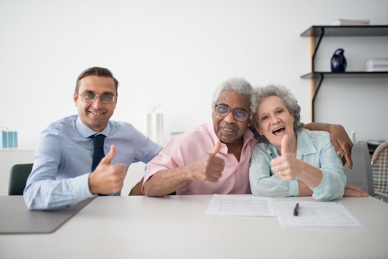 Elderly couple with consultant giving thumbs up in an office setting, showcasing positive interaction.